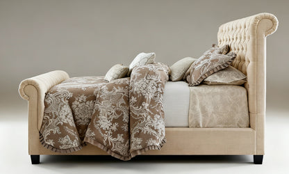 Beige upholstered bed with floral-patterned blanket and pillows on a neutral background